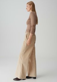 Top beige a maniche lunghe in maglia abbinato a pantaloni larghi in corduroy a vita alta. L'outfit presenta una vestibilità comoda e sottili dettagli di texture.