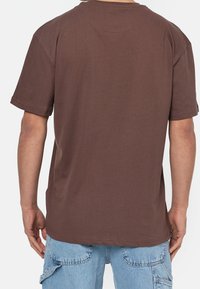 Brązowa bawełniana koszulka z krótkim rękawem, luźny krój i okrągły dekolt. Prosty design, brak widocznych logo lub wzorów.