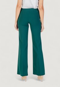Pantaloni verdi a zampa d'elefante con vita alta, texture liscia e design semplice e pulito. Presentano una zip nascosta e tasche posteriori.