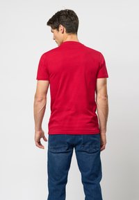 Tricou roșu din bumbac cu mâneci scurte, decolteu rotund și o siluetă ajustată, asortat cu blugi albaștri din denim care au buzunare pe spate.