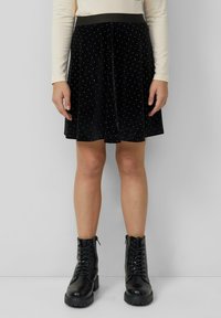 Zwarte fluwelen rok met een geplooid ontwerp en witte stippen, gecombineerd met zwarte veterschoenen tot de enkel.