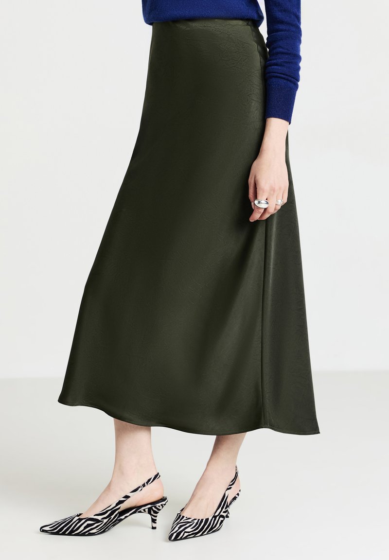 Jupe midi en satin vert olive avec une texture lisse, associée à des talons slingback noir et blanc à rayures avec un design à bout pointu.