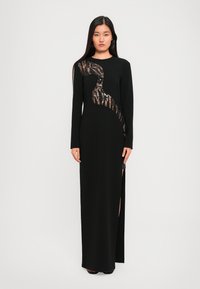 Zwart langemouwen jurk met een ontwerp van pailletten en een doorzichtige paneel, met een zijsplit voor extra detail en een gladde textuur.