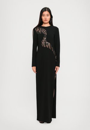 Robe noire à manches longues avec un design en sequins et panneaux transparents, dotée d'une fente sur le côté pour un détail supplémentaire et une texture lisse.