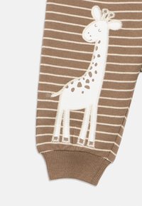 Καφέ και μπεζ ριγέ παιδικό παντελόνι με ένα λευκό και καφέ κεντητό σχέδιο καμηλοπάρδαλης στο πόδι.