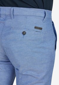 Lichtblauwe linnen broek met een gestructureerde afwerking, voorzien van een enkele zwarte knoop en gestikte labeldetail op de achterzak.