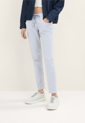 Pantalon rayé bleu clair avec une ceinture à cordon et des poches avant. Associé à des baskets blanches et une chemise en denim foncé.
