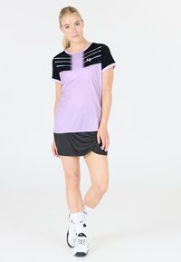 Lilla trænings T-shirt med sorte detaljer, der har vandrette striber over brystet, og en sort kort nederdel. Bæres med hvide sneakers og sokker.
