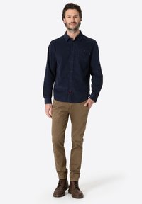 Navy button-up shirt with front pocket, corduroy texture. Tan chinos, straight fit. Brown lace-up boots with round toe and textured sole.