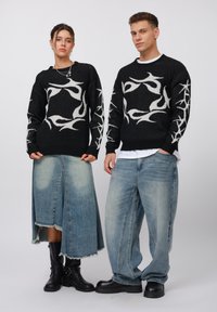 Maglioni neri a maglia con motivi di fiamme bianche, abbinati a gonne in denim azzurro chiaro e jeans larghi, completati da stivaletti neri alla caviglia.