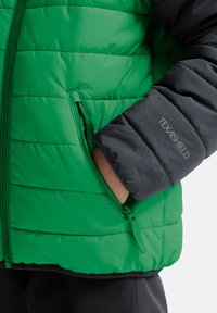 Grüne und schwarze isolierte Jacke mit gestepptem Design, Frontreißverschluss, Seitentaschen und Texashield-Logo auf dem linken Ärmel.