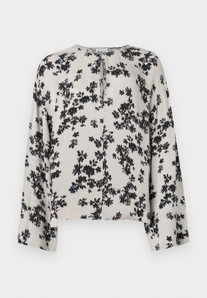 Blouse beige à manches longues avec imprimé floral noir, col rond et une petite découpe en forme de clé au centre devant.