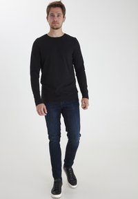 Sort langærmet t-shirt, slim fit. Båret med mørkeblå jeans og sorte sneakers med hvide såler. Ensartet design, ingen mønstre.