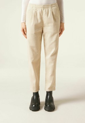 Beige corduroy pants with an elastic waistband, side pockets, and tapered ankles, paired with black ankle boots on a neutral background.