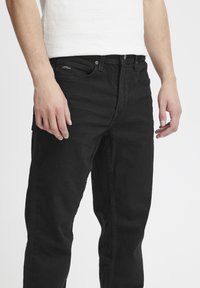 Black denim jeans with a straight fit, featuring a five-pocket design, belt loops, and a small brand label on the front pocket.