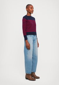 Laivastonsininen ja punaraitainen neulepaita, jossa on pyöreä kaula-aukko, yhdistettynä vaaleansinisiin korkeavyötäröisiin farkkuihin ja ruskeisiin nilkkureihin.