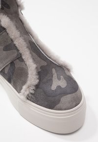 Sneaker grigio con motivo camouflage realizzato in pelle scamosciata, rifinito con pelo sintetico, punta rotonda e suola in gomma bianca con superficie texturizzata.