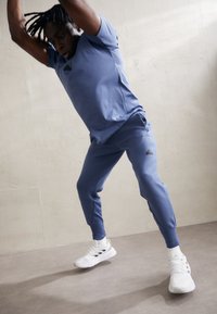 Męski strój sportowy w jasnoniebieskim kolorze, składający się z dopasowanej koszulki z krótkim rękawem oraz zwężających się spodni. Teksturowana tkanina i kontrastowe białe buty.