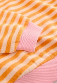 Tissu doux avec des rayures horizontales orange et blanches, avec des poignets et un ourlet côtelés roses d'un pull ou vêtement.