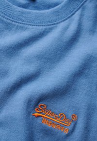 T-shirt in cotone azzurro chiaro con logo "SuperDry" ricamato in arancione e dettaglio sottolineato curvo. Texture liscia con scollatura a girocollo.