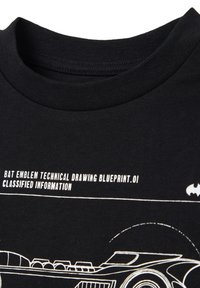 Camiseta de algodón negra con texto gráfico blanco e ilustraciones de un emblema de murciélago y un diseño de vehículo, con cuello redondo y mangas cortas.