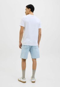 Camiseta blanca de manga corta con cuello redondo, combinada con pantalones cortos de mezclilla azul claros, calcetines de color neutro y zapatillas blancas con suelas marrones.