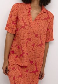 Korte mouwen overhemd in fel oranje met een rood bladraster. Heeft een kraag en een relaxte pasvorm, gemaakt van lichte stof.