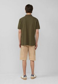 Dunkelgrünes Poloshirt, beige Cargo-Shorts mit seitlichen Taschen und weiße Sneakers mit dunklen Akzenten. Schlichtes, lässiges Design.