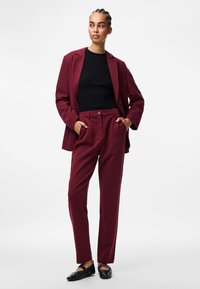 Burgundy skräddarsydd kavaj och byxset, med en svart ribbad topp. Kavajen har en notch-krage och byxorna är något avsmalnande. Svarta flats.