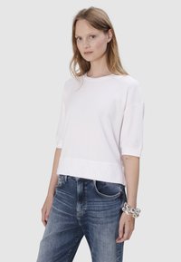 Witte kortemouwen top met een ronde hals en ribgebreide manchetten, gedragen met blauwe versleten jeans, die een relaxte pasvorm en een soepele textuur tonen.