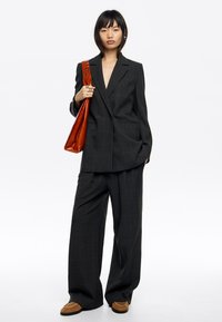 Blazer de cuadros negros oversize con pantalones anchos a juego. El modelo lleva un bolso de cuero marrón y calza zapatos marrones.