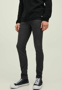 Mørkegrå slim-fit jeans laget av denim, kombinert med en svart fleecegenser og svarte joggesko med hvite såler og snøringer. Rent design, minimal detaljering.
