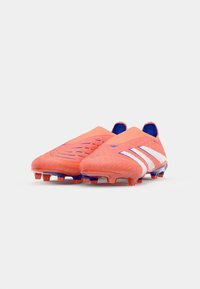 Botas de fútbol de color naranja brillante con un acabado texturizado, que cuentan con rayas blancas y acentos azules. Diseño de tipo slip-on con tacos moldeados para tracción.