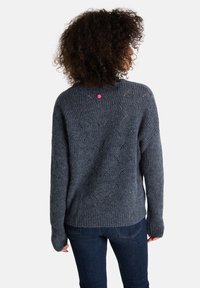 Grauer gestrickter Pullover mit einem strukturierten Muster, ausgestattet mit einem gerippten Saum und einem rosa Etikett am Rücken. Lange Ärmel und lockere Passform.
