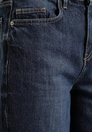 Zbliżenie ciemnoniebieskich dżinsów z widoczną przednią kieszenią, kieszonką na monety z pomarańczowym przeszyciem i srebrnym nitom na fakturze tkaniny.