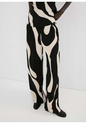 Pantalones de pierna ancha con patrón abstracto en blanco y negro, usados con zapatos negros sobre un fondo claro y liso.