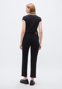 Μαύρο κοντό t-shirt με λευκή επένδυση, συνδυασμένο με μαύρο τζιν ψηλόμεσο. Διακριτική δερμάτινη ετικέτα πίσω. Λείο ύφασμα, άνετη εφαρμογή.