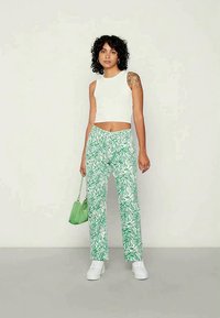 Top cropped branco, calças verdes com padrão e ténis brancos, acompanhado por uma pequena mala verde. Tecido suave, design de pernas retas.