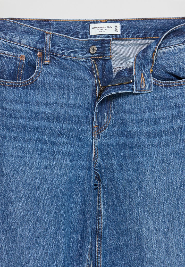 Blaue Denim-Jeans mit niedrigem Bund, ausgestattet mit einem Reißverschluss, einem Knopfverschluss und orangefarbenen Nähten. Enthält Vordertaschen und ein Lederetikett am Bund.