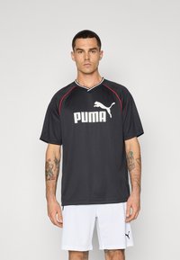T-shirt de sport Puma noir avec des accents rouges, à manches courtes et col en V ; présente un logo blanc prominent à l'avant.