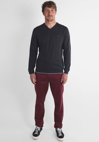Un pull v-neck bleu foncé, à manches longues, associé à un pantalon bordeaux. Des baskets noir et blanc. Design simple, couleurs unies, coupe décontractée.
