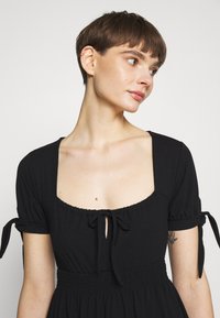 Vestido preto com decote quadrado, mangas curtas bufantes com laços e cintura elástica para um ajuste justo.