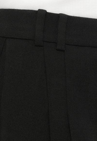 Pantaloni negri dintr-un material texturat, având un talie cu curea și pliseuri frontale curate. Prim-planul pune accent pe țesătura materialului.
