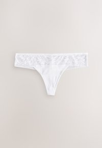 String en dentelle blanche avec broderie florale et détails en mesh, posé à plat sur un fond beige clair.