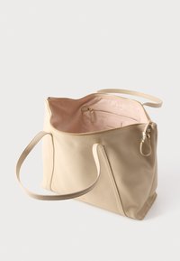 Τσάντα χειρός από μπεζ δέρμα με μακριές λουρίδες, ανοιχτό φερμουάρ που αποκαλύπτει απαλό ροζ ύφασμα στο εσωτερικό με μια μικρή τσέπη με φερμουάρ μέσα.