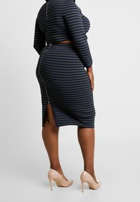 Striped, navy and olive two-piece outfit featuring long sleeves, a fitted crop top, and a pencil skirt with a side slit and zipper detail.