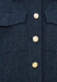 Tummansininen farkkupaita, jossa on kultaiset napit, kaksi rintataskua ja suora leikkaus. Kangas on sileäpintaista ja hieman kiiltävää.