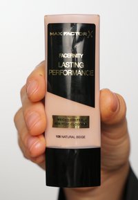 Fond de teint Max Factor Facefinity Lasting Performance dans un tube rose clair avec des accents noirs, portant une étiquette dorée indiquant "sensation légère, non comédogène" et "106 Beige Naturel."