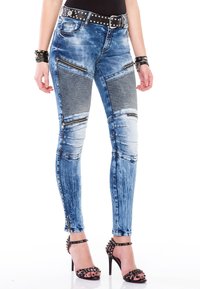 Vaqueros ajustados de mezclilla, con un color azul desgastado, bolsillos con cremallera, detalles acanalados en las rodillas y cremalleras en los tobillos.