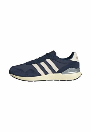 Marineblauer Adidas-Sneaker mit weißen Streifen, beiger Sohle und silbernem Fersenakzent, von der Außenseite auf weißem Hintergrund gezeigt.